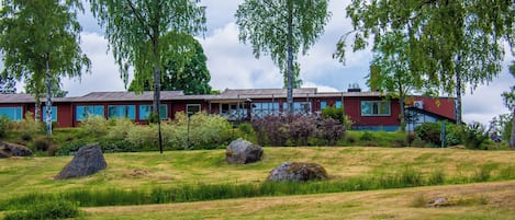 Un edificio moderno con fachada roja, rodeado por una zona verde con rocas grandes y árboles.