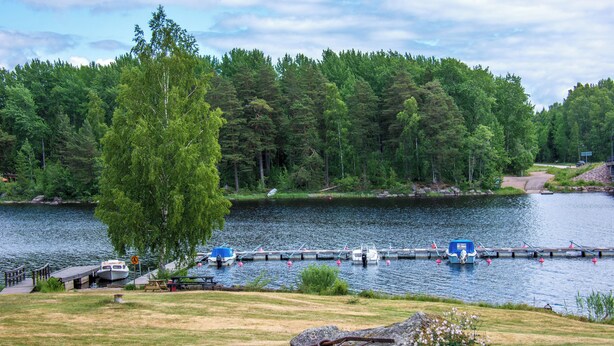 A lakeside dock with boats, a picnic area, and a forested backdrop. - Lungsunds hotell & camping (Storfors)