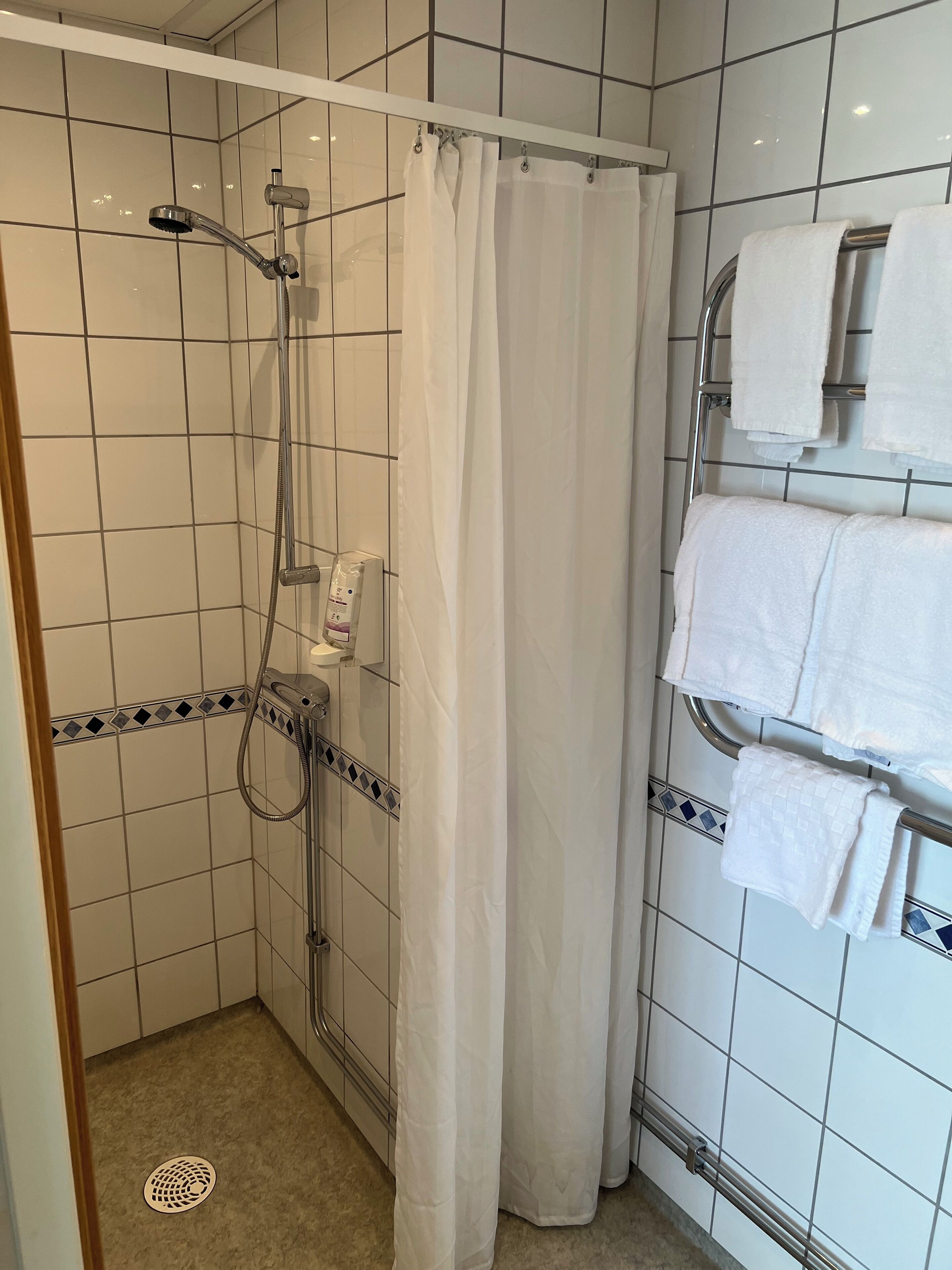 Zona de ducha con cabezal, cortina y toallero con toallas.