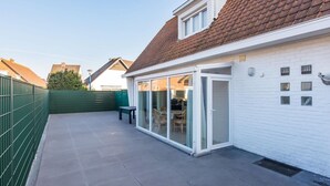 A residential property with a covered patio, a sliding glass door leading to an indoor area, and a green fence. - Villa in Koksijde Near the Sea (Koksijde)