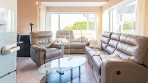 A modern living room with leather sofas, a glass coffee table, and large windows offering a view of the outdoors. - Villa in Koksijde Near the Sea (Koksijde)
