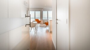 Un couloir moderne et bien éclairé, avec vue sur un balcon, qui mène à un coin repas agrémenté de chaises orange et d’une table blanche.