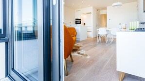 Un intérieur moderne avec une porte vitrée, un coin cuisine, un espace repas et un salon comprenant un canapé et des fauteuils.