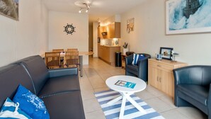 Uma sala de estar moderna com um sofá, uma mesa de jantar e uma área de cozinha ao fundo.