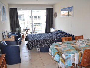 A hotel room with a bed, a dining table, chairs, a TV, and a balcony with curtains. - Studio in St-idesbald With Sea View Balcony (Koksijde)