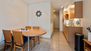 Uma cozinha compacta com armários de madeira, painel de azulejos e uma pequena lixeira.
