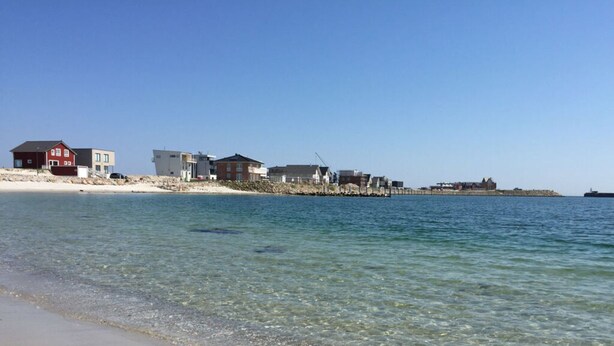 A beach with clear water, sandy shore, and buildings in the background. - Holiday Home on the Baltic Sea (Kappeln)