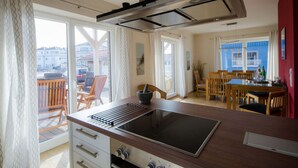 A modern kitchen with a large island, sliding glass doors leading to a balcony, and a dining area with wooden furniture. - Holiday Home on the Baltic Sea (Kappeln)