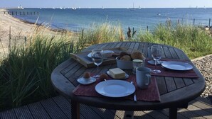 A wooden table with plates, glasses, and food items set for a meal overlooking a beach with sailboats in the distance. - Holiday Home on the Baltic Sea (Kappeln)
