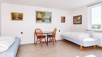 Una habitación con dos camas individuales, una pequeña mesa con sillas y tres cuadros en la pared.