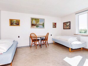 A room with two single beds, a small table with chairs, and three framed pictures on the wall.
