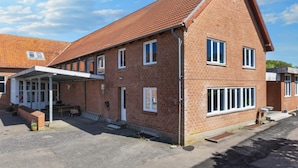 A two-story brick building with a sloped roof, a covered outdoor seating area, and a paved driveway. - 12 Person Holiday Home in Roslev (Roslev)