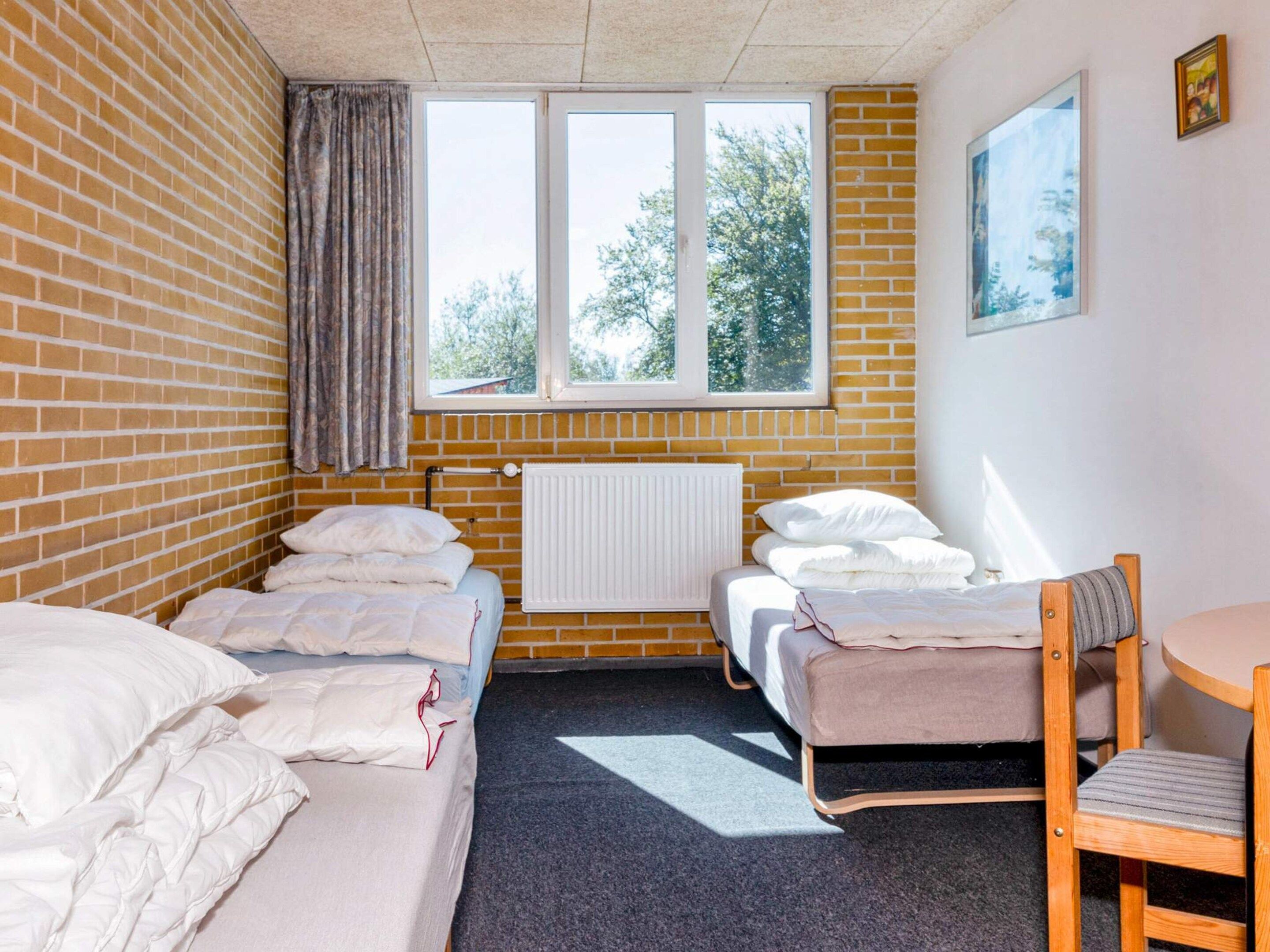 A room with two beds, a radiator, a window with a view of trees, and a chair.