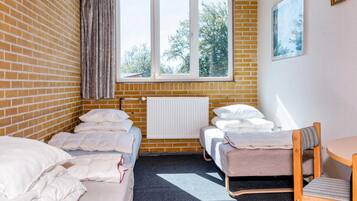 A room with two beds, a radiator, a window with a view of trees, and a chair.