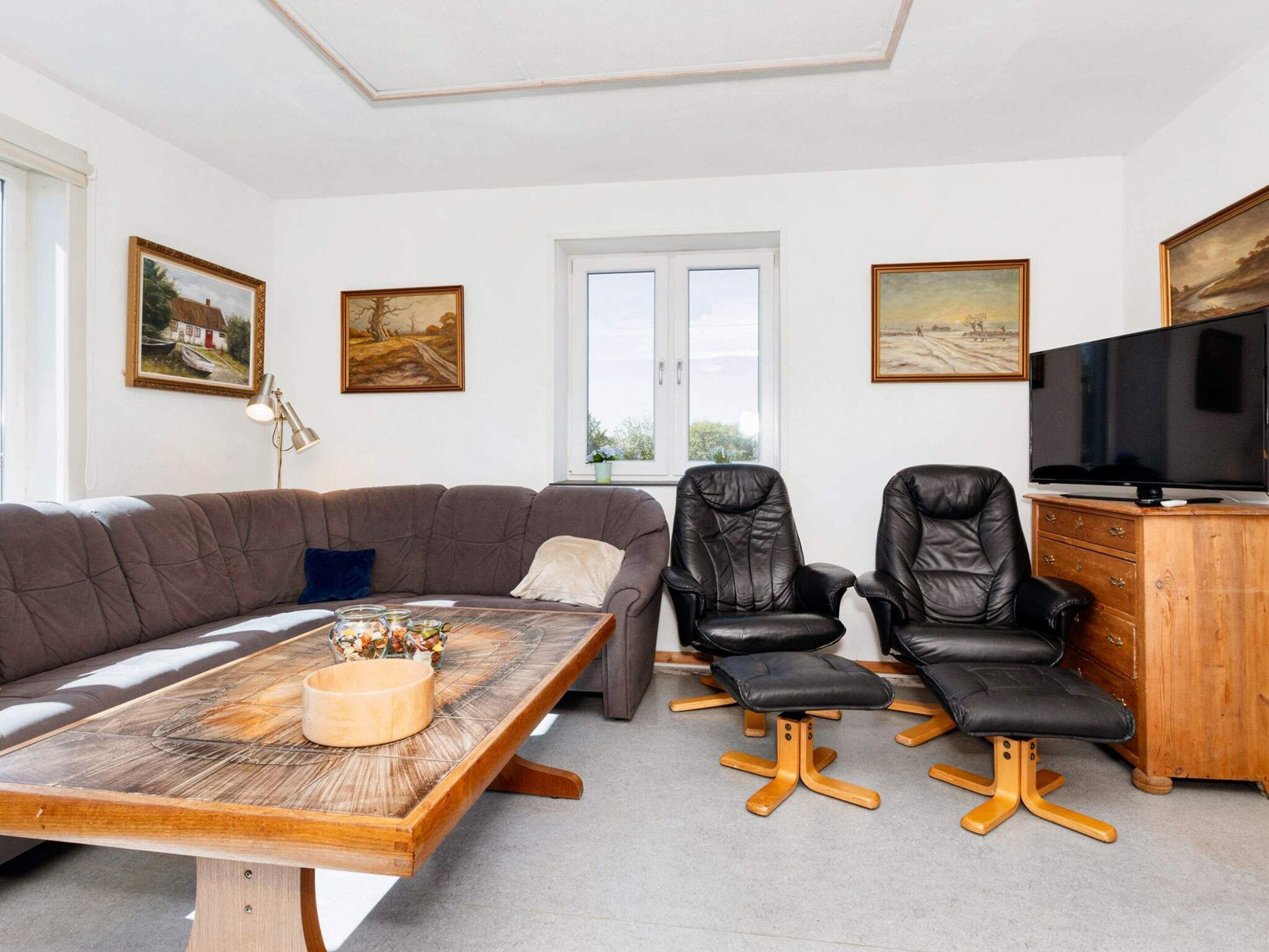 A living room with a sofa, two chairs, a wooden coffee table, a television, and artwork on the walls.