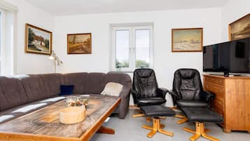 A living room with a sofa, two chairs, a wooden coffee table, a television, and artwork on the walls.
