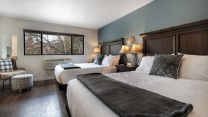 Hotelkamer met twee bedden, een groot raam, een stoel en een nachtkastje met lampen.