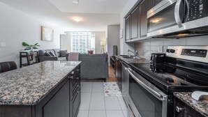 A modern kitchen with granite countertops, stainless steel appliances, and a grey sofa in the adjacent living area. - Spacious 3bed/2 bath Downtown Toronto condo + Free Parking, min to CN tower (Toronto)