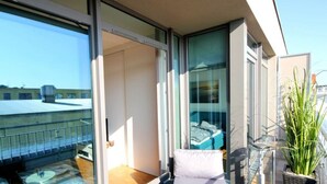 Een balkon met een glazen deur, een comfortabele stoel en een pot met een plant.