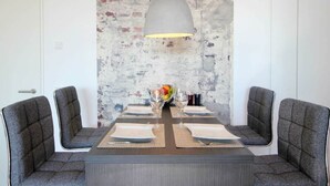 Een eethoek met een rustieke bakstenen muur, een centrale tafel met vier stoelen en een hanglamp.
