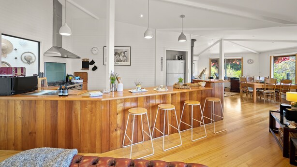 Une cuisine moderne avec des tabourets de bar en bois, un coin repas doté d’une grande table et une vue sur l’extérieur.