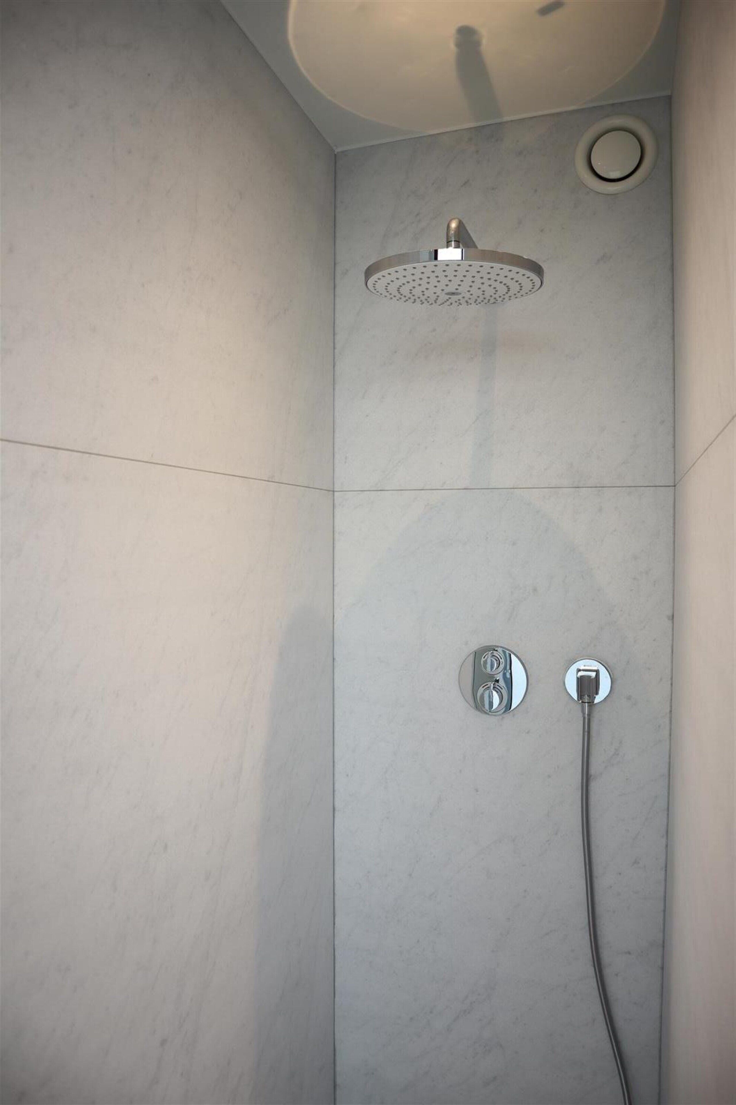 Ducha en esquina con cabezal de ducha de mano y panel de control en la pared.