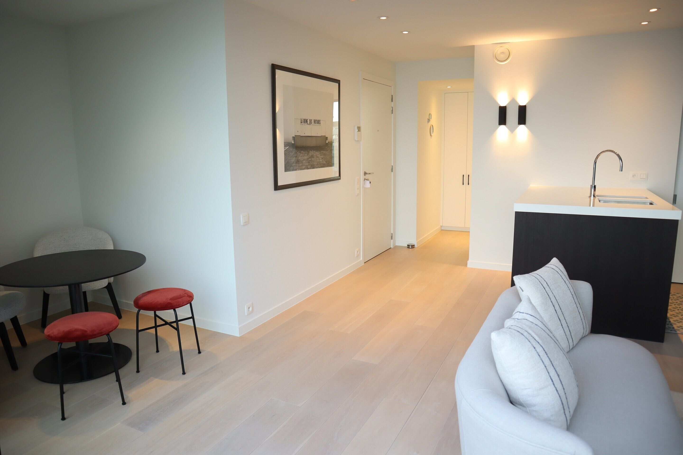 A modern living room with a sofa, a dining table with two chairs, and a kitchen area with a sink and countertop.