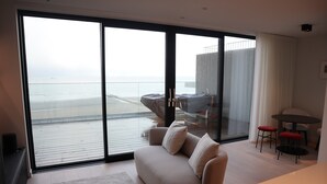 A modern living room with a large sliding glass door leading to a balcony overlooking a beach.