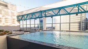 An indoor swimming pool with a glass enclosure, a blue metal frame, and a city view. - Family-friendly Dallas getaway with rooftop pool, free parking & Texas flair. (Dallas)