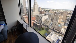 A room with a large window offering a city view, a gray sofa, and a small table. - Family-friendly Dallas getaway with rooftop pool, free parking & Texas flair. (Dallas)