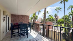 A balcony with a brick wall, two blue chairs, a patterned rug, and a view of palm trees and buildings. - Villa del Sol - #205 (South Padre Island)