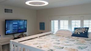 A bedroom with a bed, a television, a window with blinds, and a wall with a sign.
