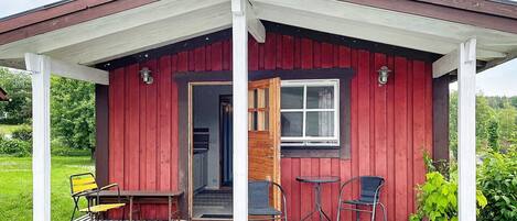 A small red wooden cabin with a porch, a door, and a window.