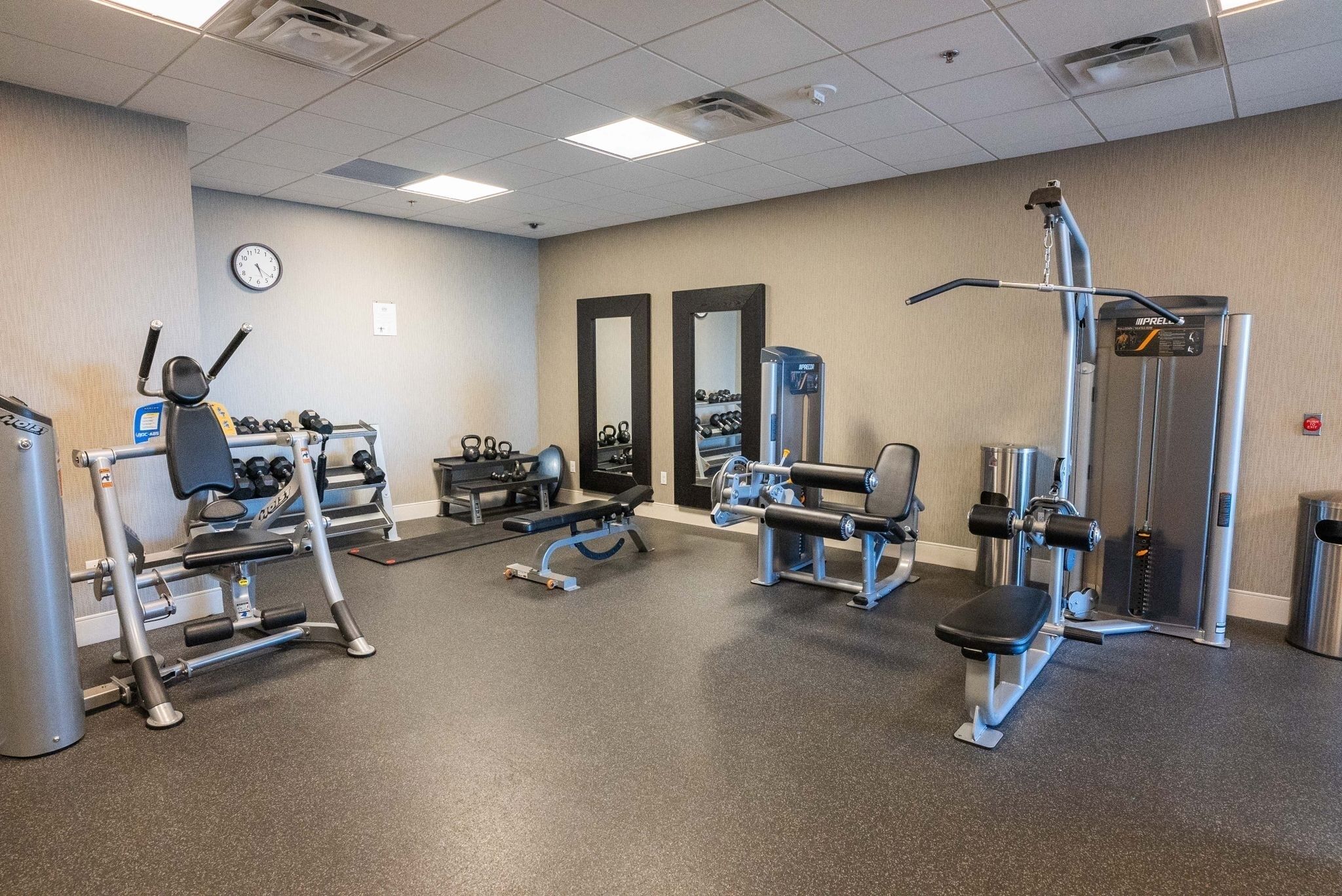 A gym with various exercise equipment, a clock on the wall, and a mirror.