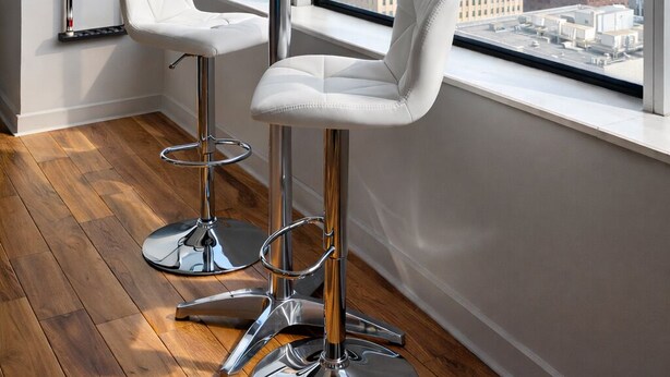 A modern room with a large window, two white bar stools, and a round table. - Cozy Retreat with Rooftop Pool, Parking, and Spacious Comfort (Dallas)