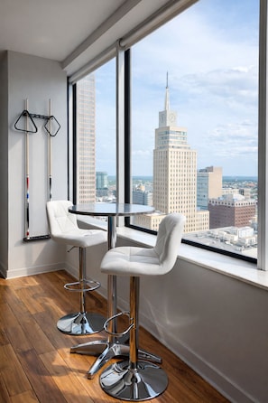 A modern room with a large window, two white bar stools, and a round table. - Cozy Retreat with Rooftop Pool, Parking, and Spacious Comfort (Dallas)