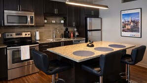 A modern kitchen with dark wood cabinets, stainless steel appliances, a granite countertop, and a bar area with stools. - Cozy Retreat with Rooftop Pool, Parking, and Spacious Comfort (Dallas)