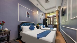 Een hotelkamer met twee bedden, een groot raam met gordijnen, een tv aan de muur en een klein tafeltje met een bloevas.