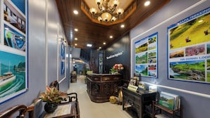 Een hotel lobby met een receptiebalie, houten meubels en wanddecoraties, waaronder reisposters.