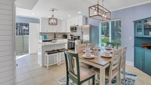 A modern kitchen with white cabinets, a central island, and a dining area with a wooden table and chairs. - Luxury Hilton Head Townhome with pool and biking distance to beach (Hilton Head Island)