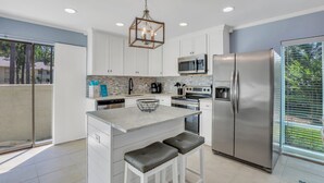 A modern kitchen with white cabinets, stainless steel appliances, a central island with stools, and a hanging light fixture. - Luxury Hilton Head Townhome with pool and biking distance to beach (Hilton Head Island)