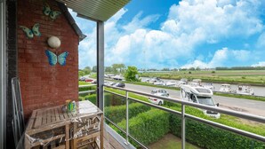 Ein Balkon mit Blick auf eine Autobahn und parkende Fahrzeuge, darunter ein Wohnwagen.