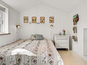A bedroom with a floral bedspread, a white dresser, a nightstand, and wall-mounted lamps.
