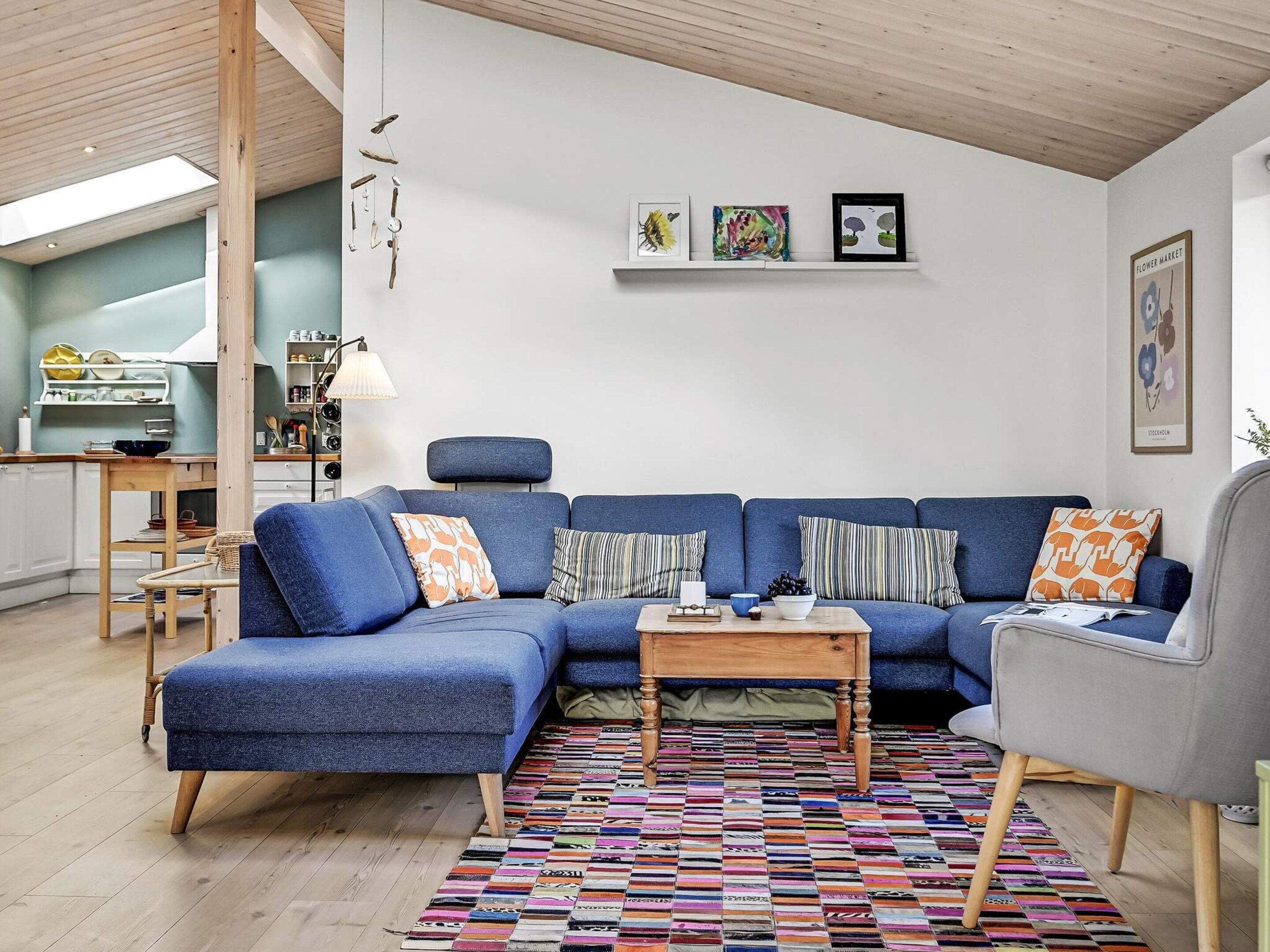A modern living room with a blue sectional sofa, a wooden coffee table, and a colorful rug.