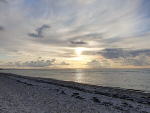A beach with a clear sky and the sun setting over the horizon.