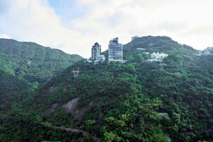 Uma área montanhosa com construções em uma colina, uma ponte e vegetação densa.