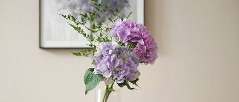 A round table with a clear vase containing purple flowers and a bowl of green grapes.