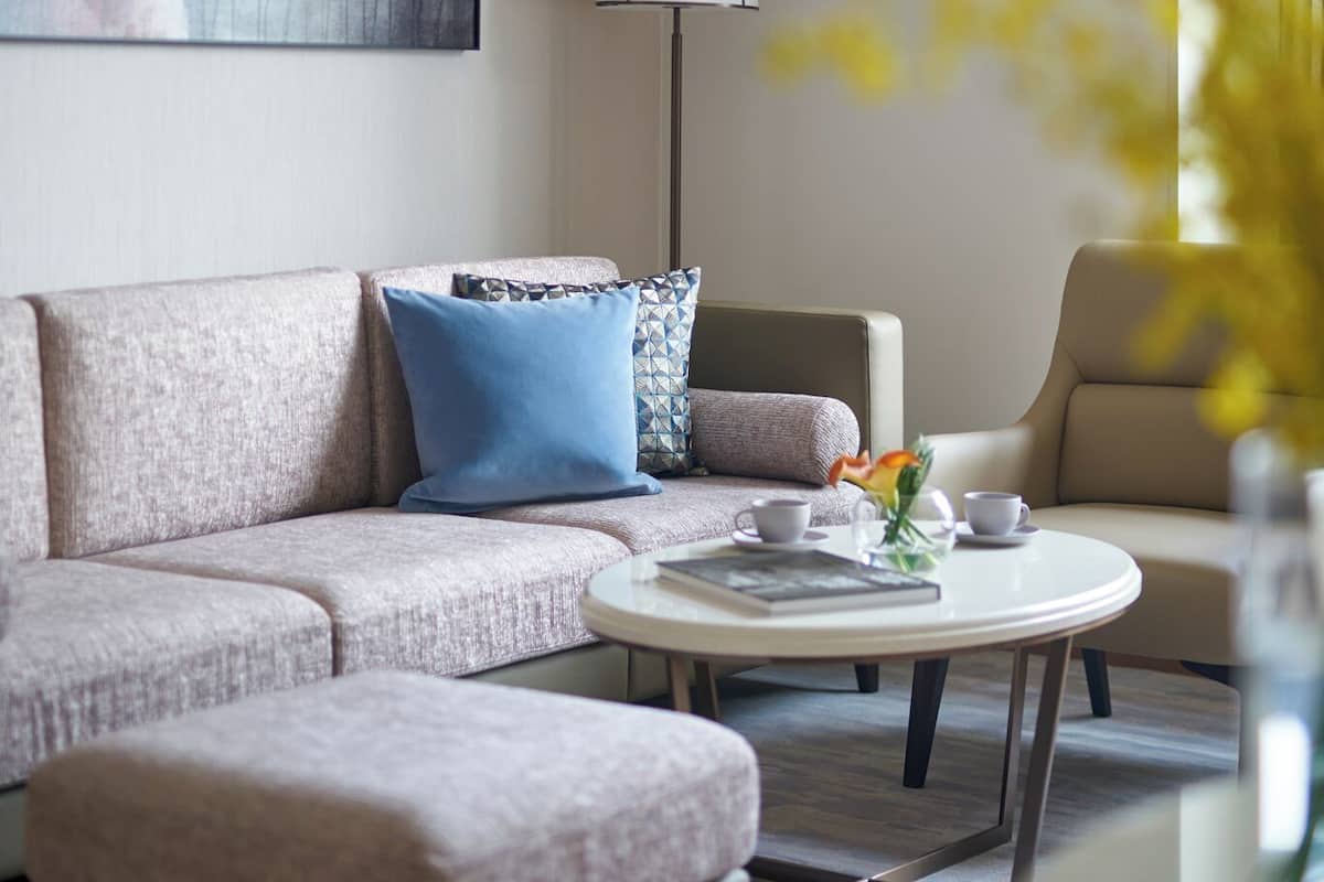 A modern living room with a sofa, ottoman, and a coffee table. There is a painting on the wall and a floor lamp.