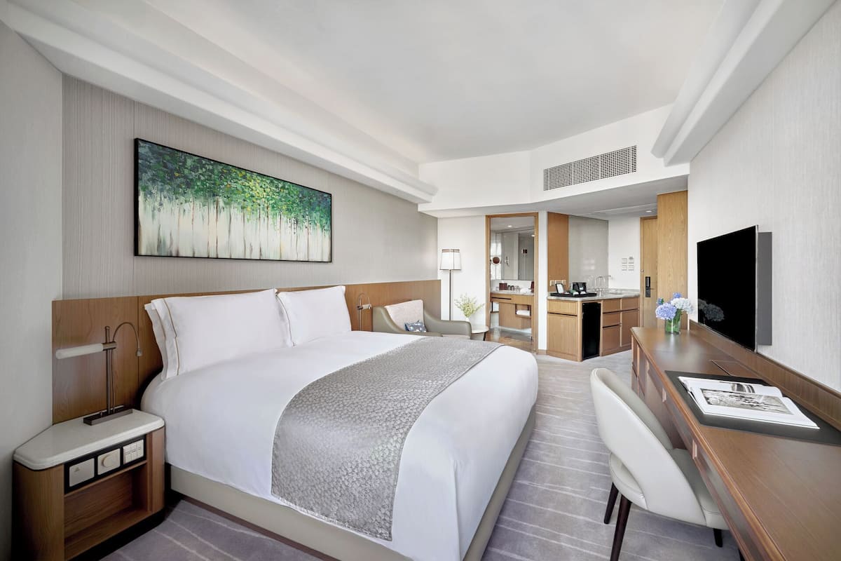 A hotel room with a large bed, a desk, a TV, and a bathroom visible through an open door.