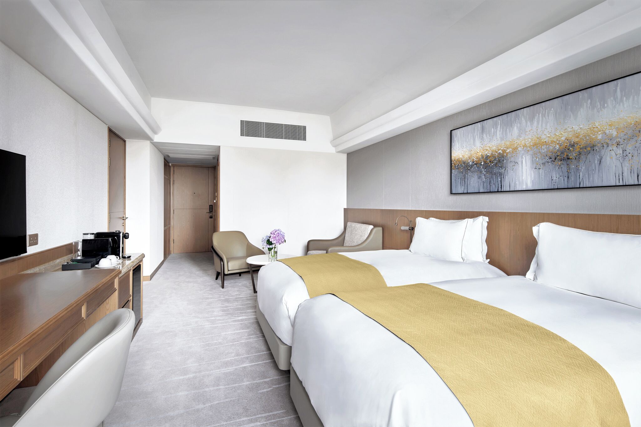 Quarto de hotel com duas camas, uma escrivaninha, uma cadeira, uma televisão e um quadro na parede.